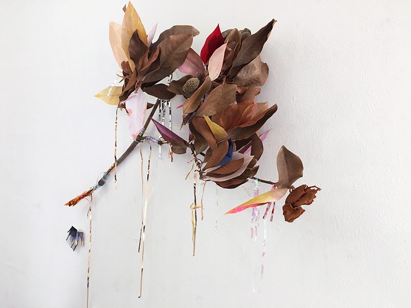 A dried magnolia branch with brwon leaves, and colorful leaves of paper and other materials.