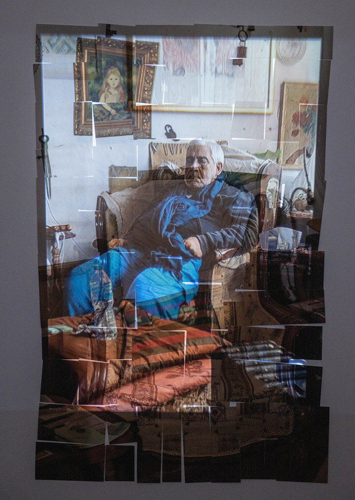 Collaged photographs forming an image of a man with white hair seated in a room crowded with furnishings.