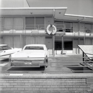 A blakc and white photograph of a motel, vintage cars parked in front.