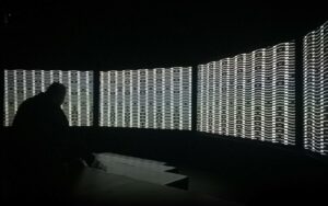A person sits in a dark room viewing a large scale abstract black and white projection.