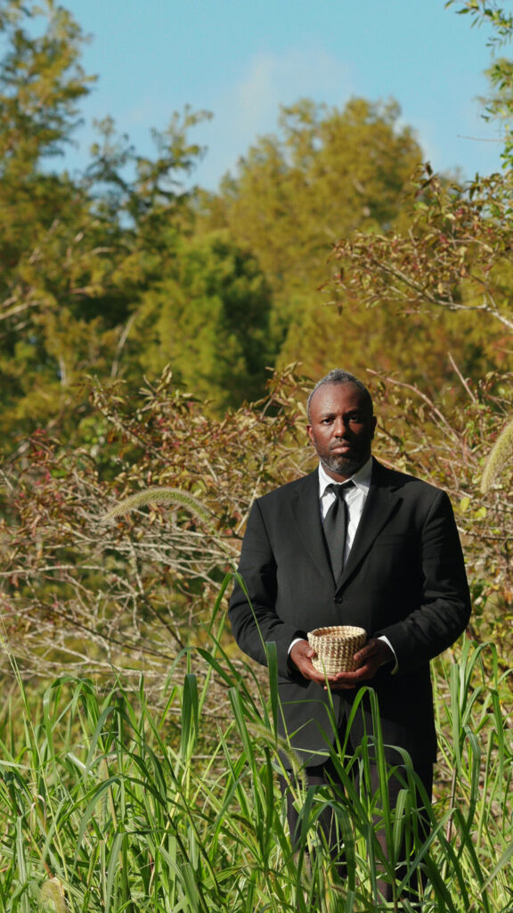 A black man standing in a field a suit holding a small basket