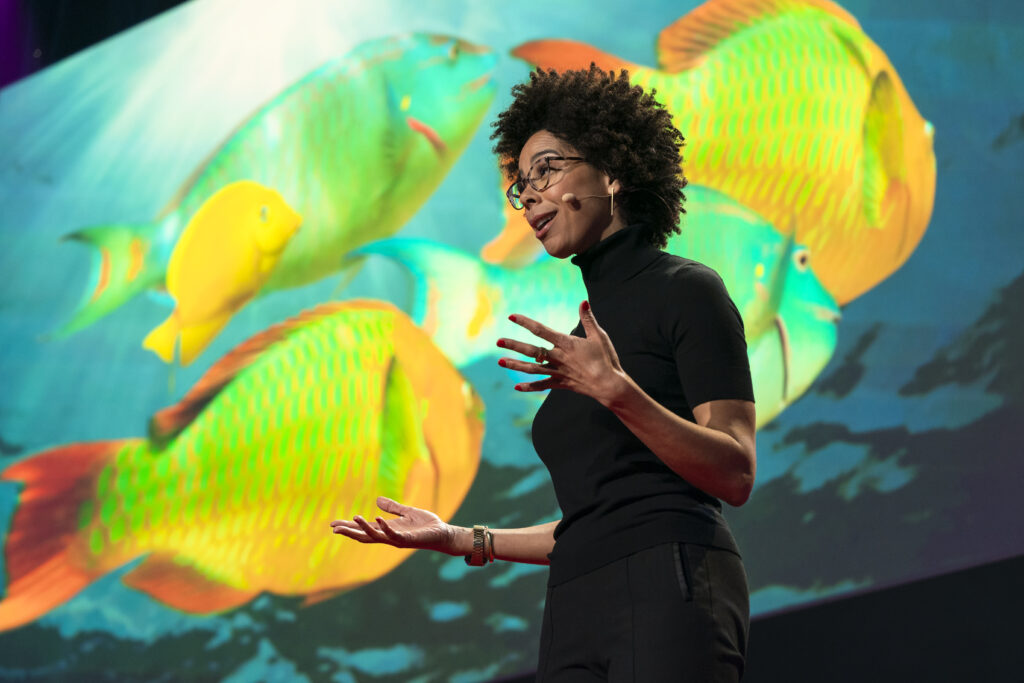 A photo of a person standing in front of a colorful image of tropical fish.