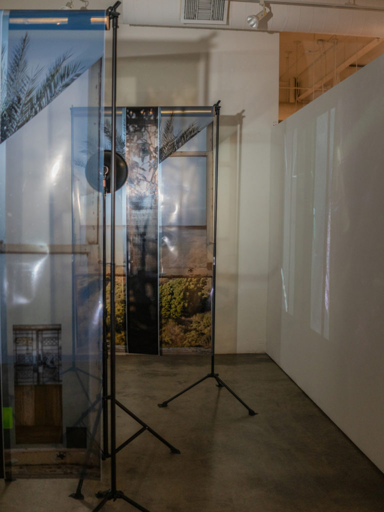 Images of windows and landscapes printed on transparency and hung overlapping from metal racks.
