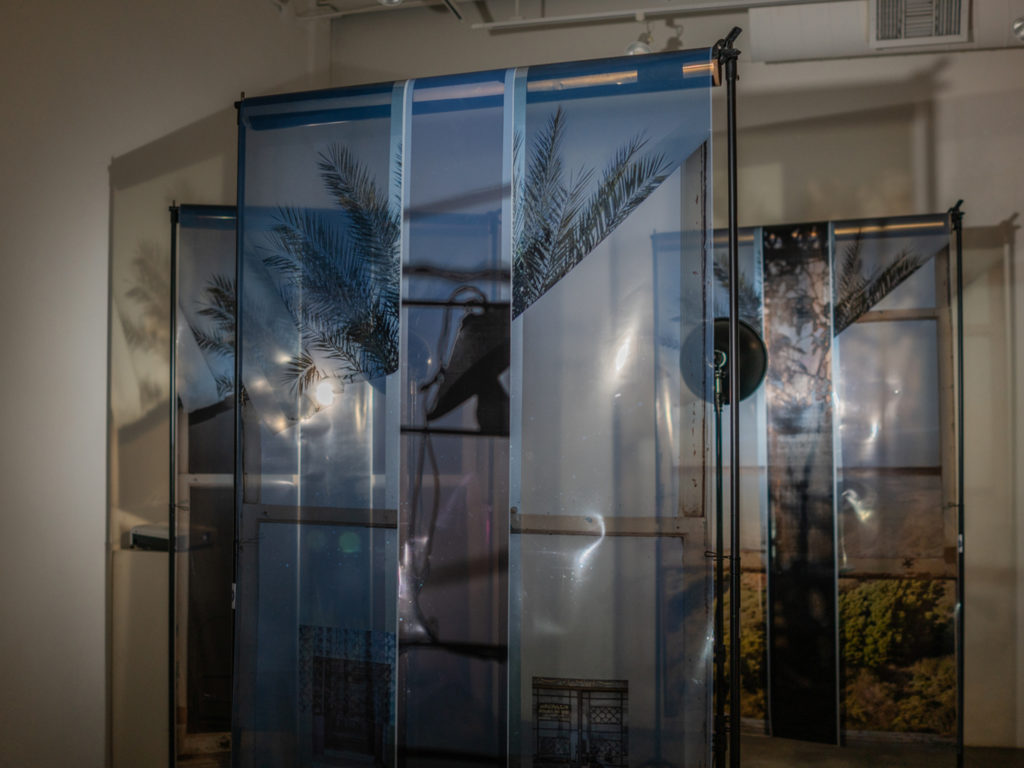 Images of windows and landscapes printed on transparency and hung overlapping from metal racks.