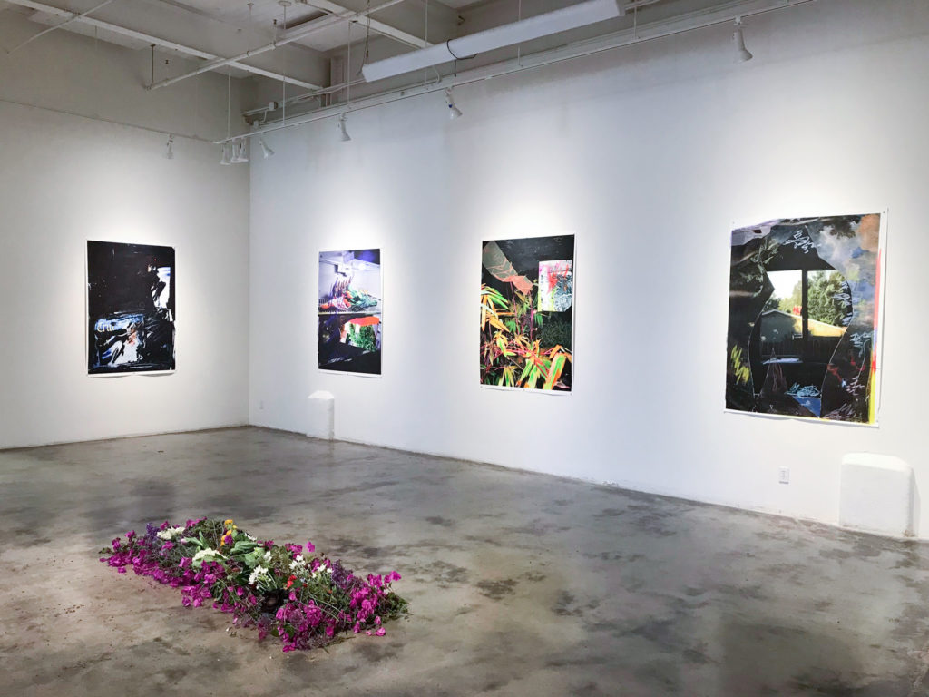 An arrangement of flowers on the floor, with wall-hung artworks behind