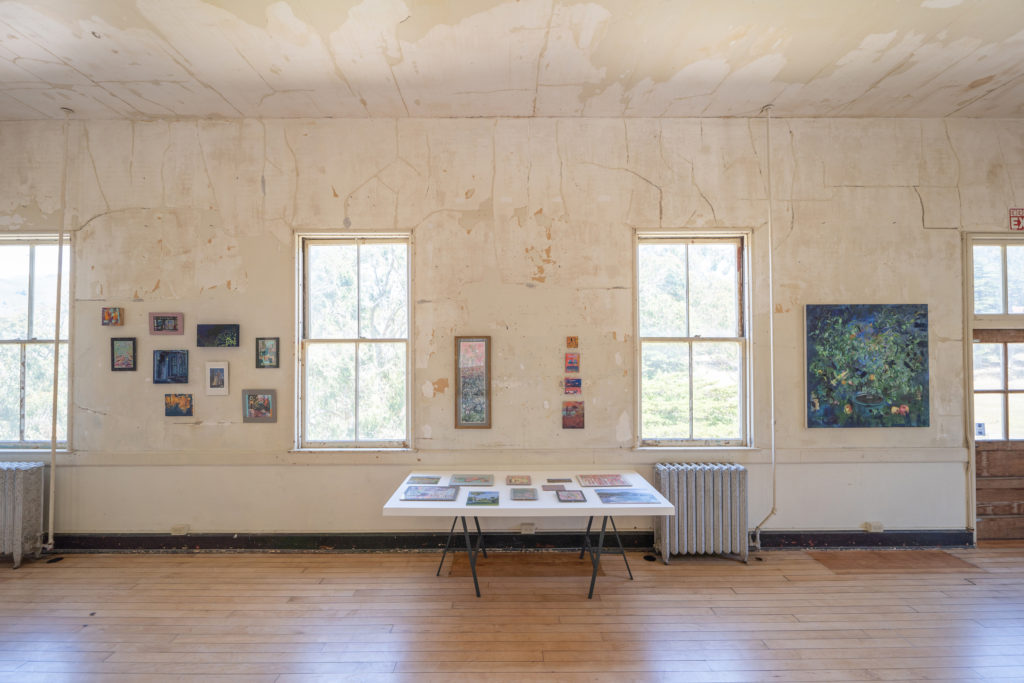 A view of a table with collages and paintings hung on the wall behind