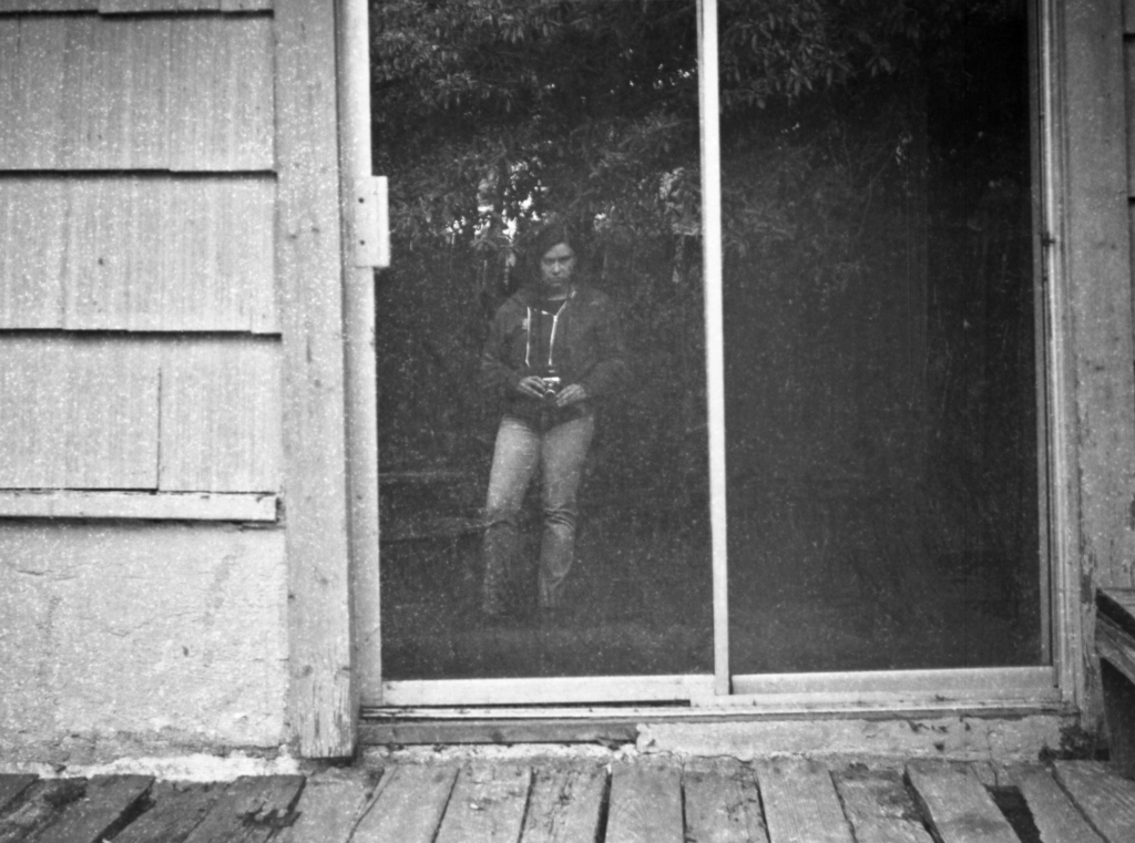 Black and white photograph with a person reflected in a sliding glass door.