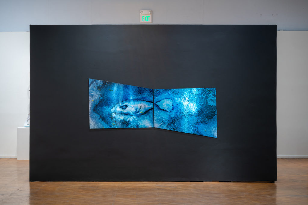 A blue abstract work hanging on a dark wall