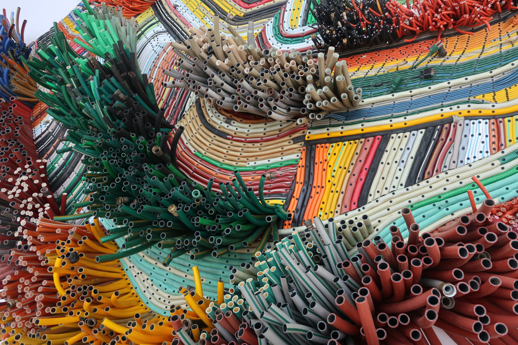 A detail of a sculpture made of plastic tubing, arranged in colored patterns reminiscent of a rug or weaving