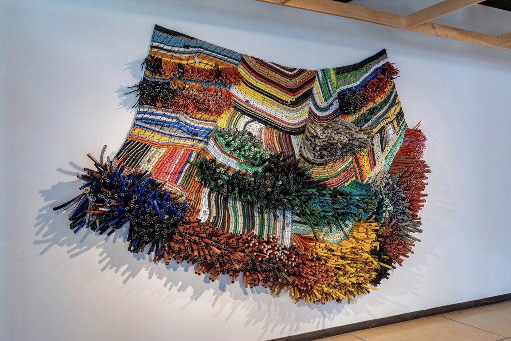A sculpture made of plastic tubing resembling a rug or weaving, hung on a wall