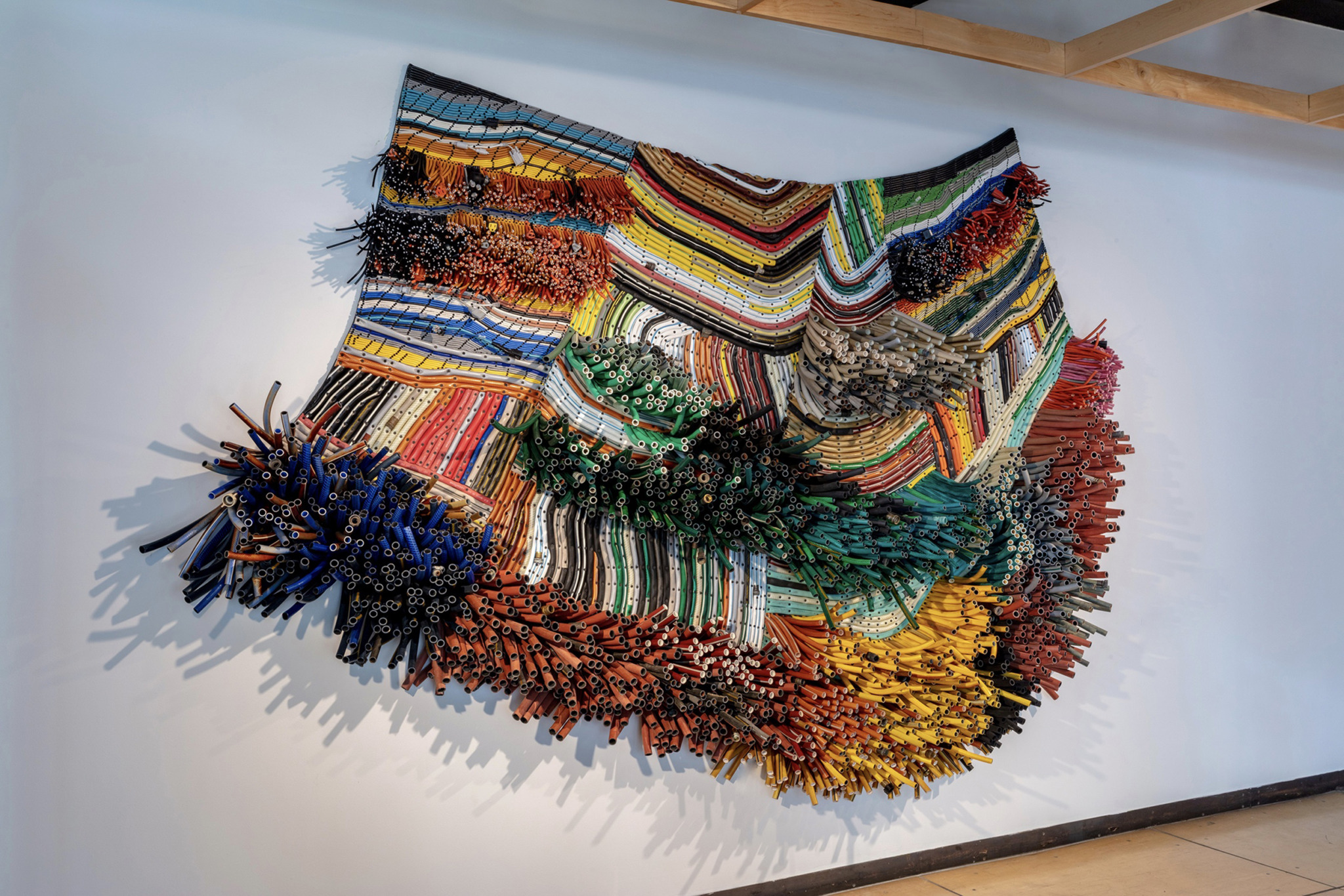 A sculpture made of plastic tubing resembling a rug or weaving, hung on a wall