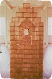 A sculpture of a house made out of brass "bricks," reflecting another house sculpture.