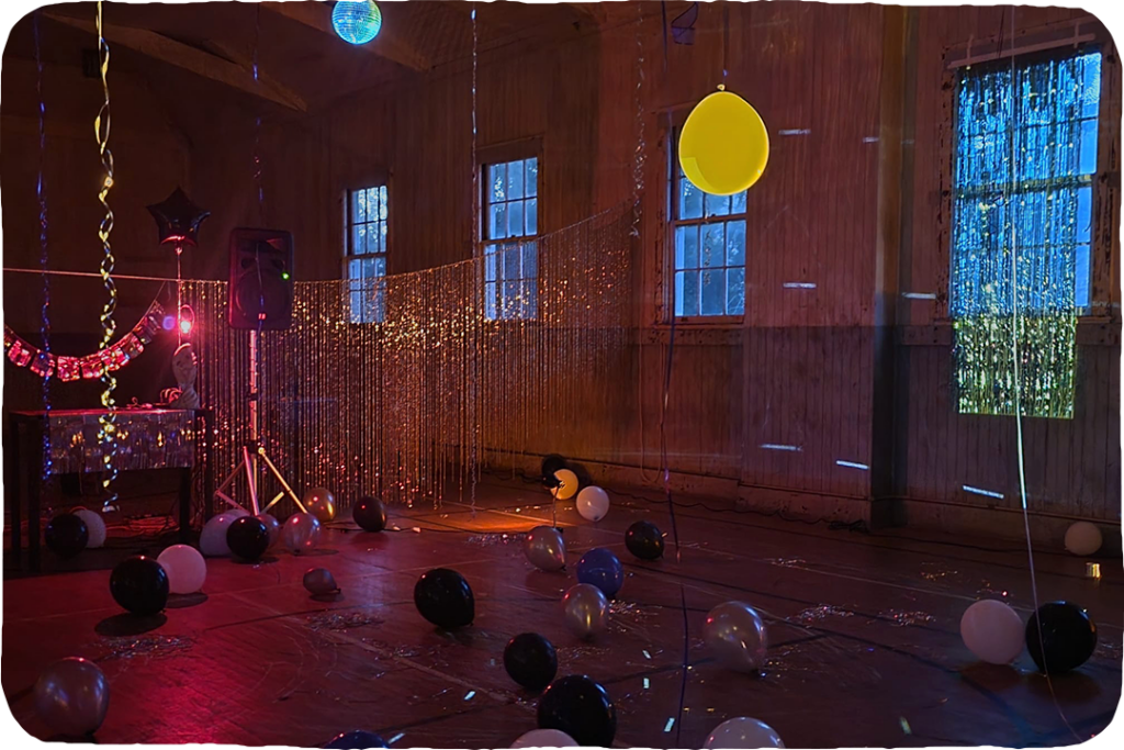 A large gymnasium room with a red floor decorated with tinsel and balloons