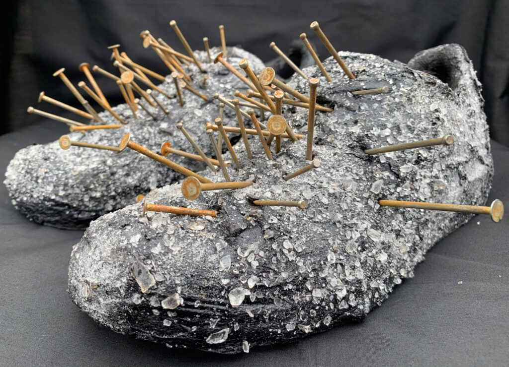 Shoes encrusted with tar and glass, with gold-hued nails