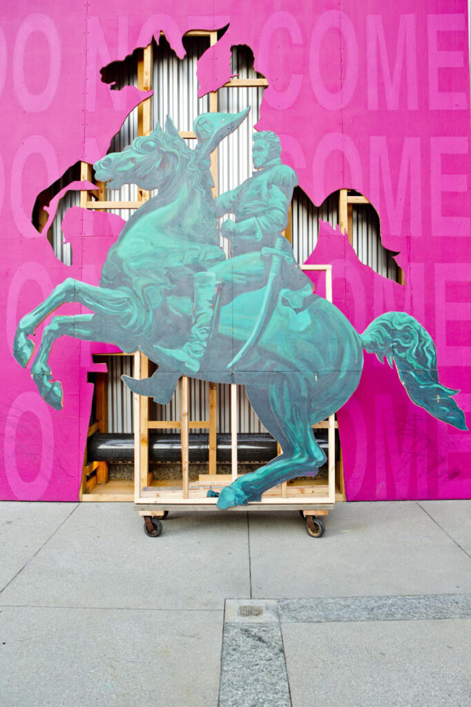 A wooden sculpture of with an image of a person on a horse against a pink wall.