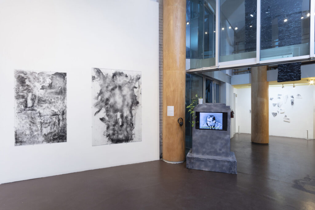 A view of a gallery with a video embedded in a gray tombstone, and two abstract black and white images.