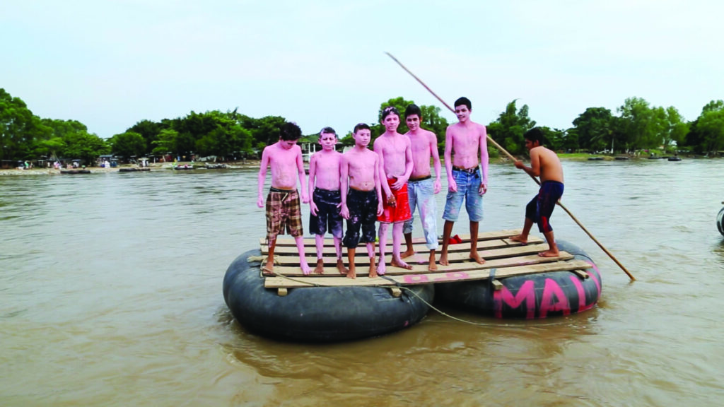 A group of children painted pink on a raft in a river.