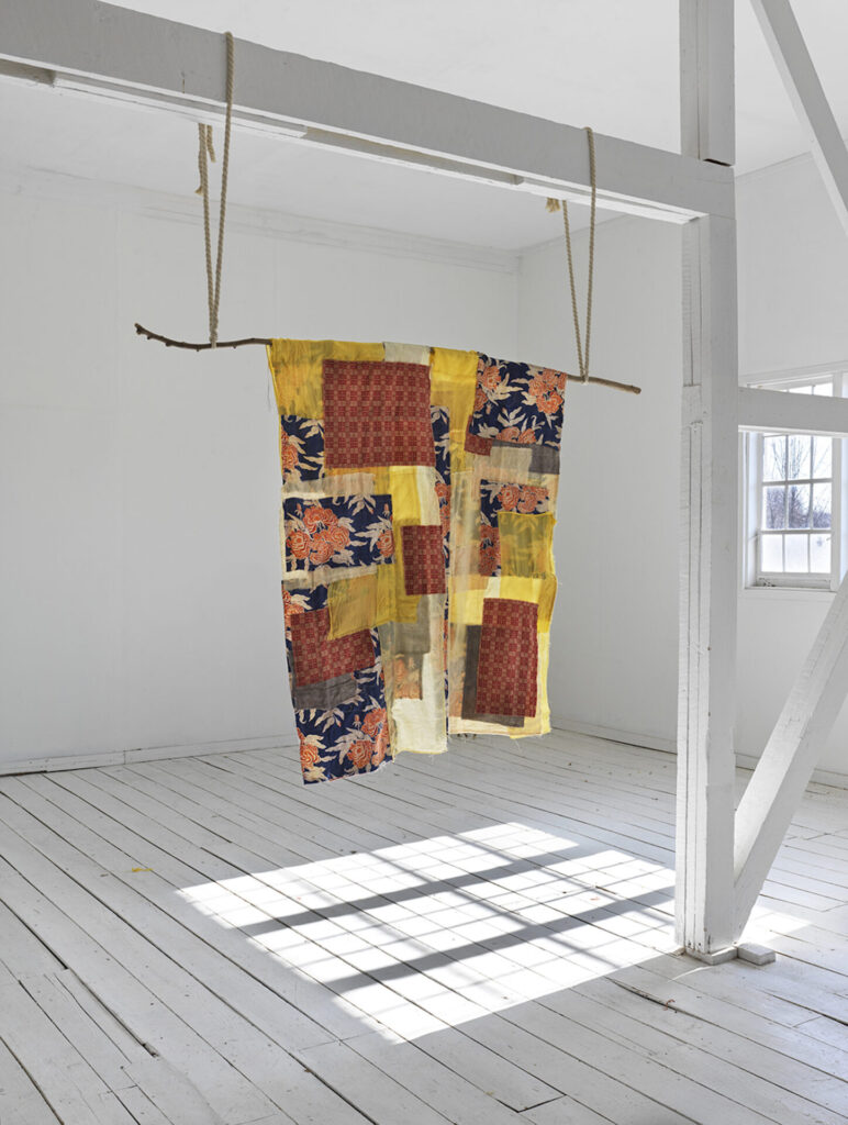A yellow and orange quilted fabric piece hanging from a rod in a white room