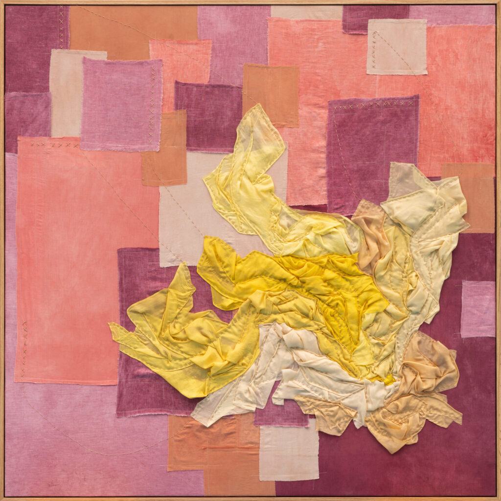 A quilted fabric work with a mass of yellow fabric in front of pink-hued squares