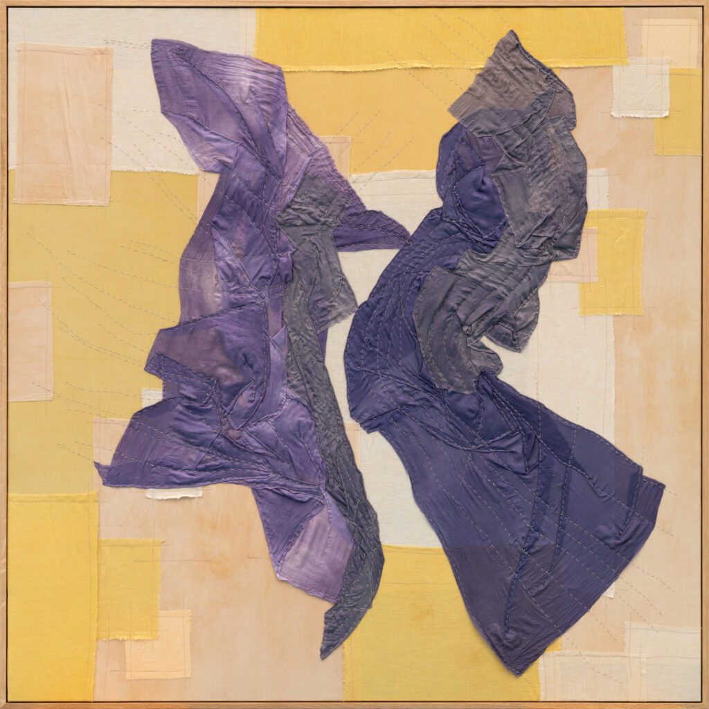 A quilted fabric work with two chunks of purple fabric overlaid on yellow tiles