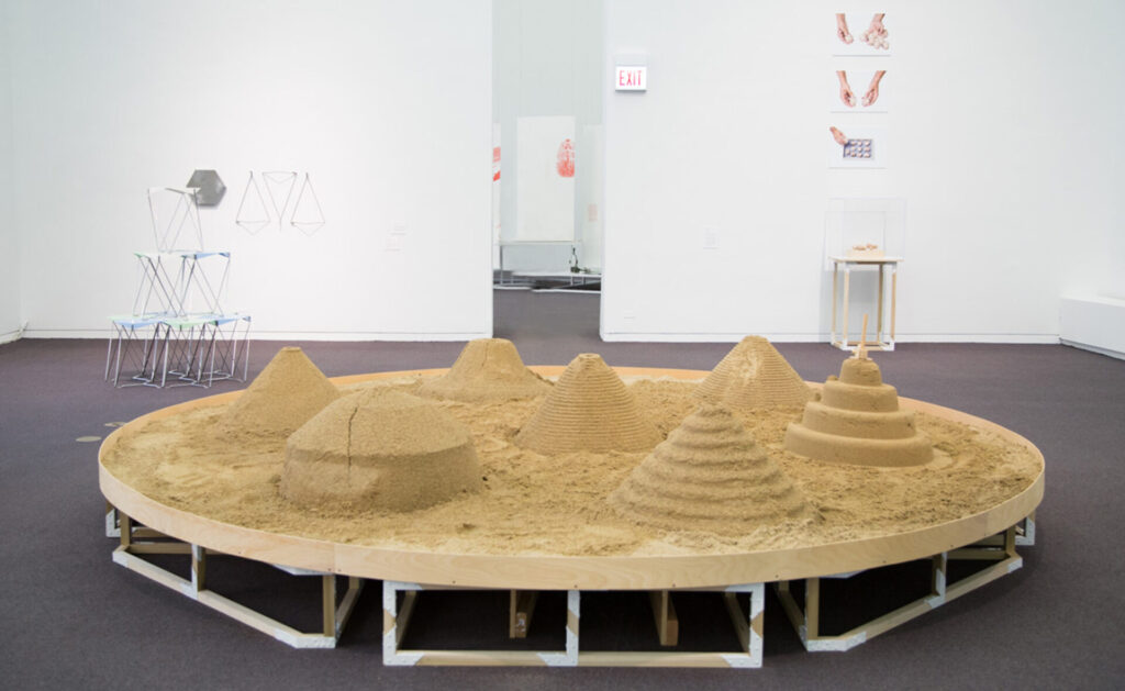 Large circular platform covered with sand, with pyrimid and mound forms made out of sand on top of it.