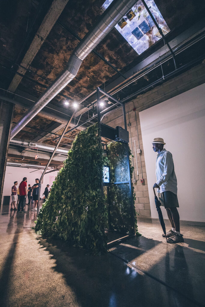 A metal staircase on casters covered in fake plants, with a video monitor set underneath