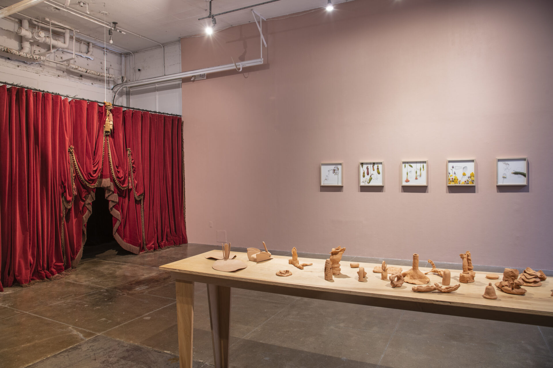 A room with a red curtain on one wall, a table with objects, and framed images