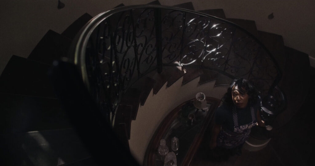 A dimly lit view down a spiral staircase and a woman looking up.