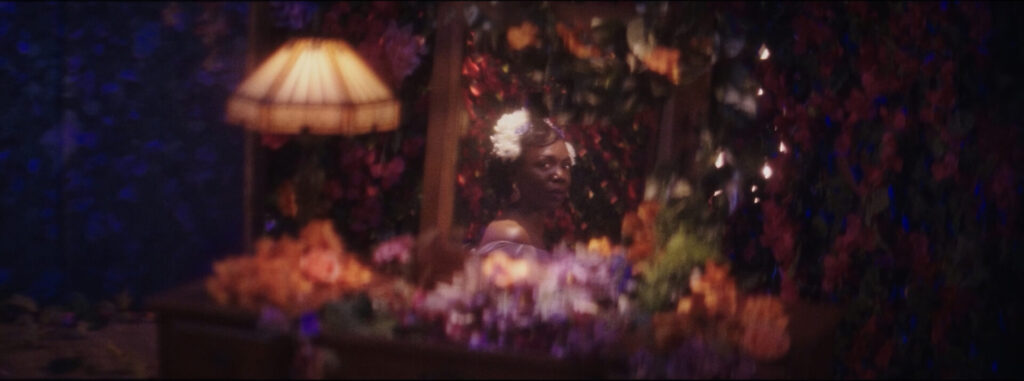 A Black woman reflected in a mittor surrounded by flowers and lamps