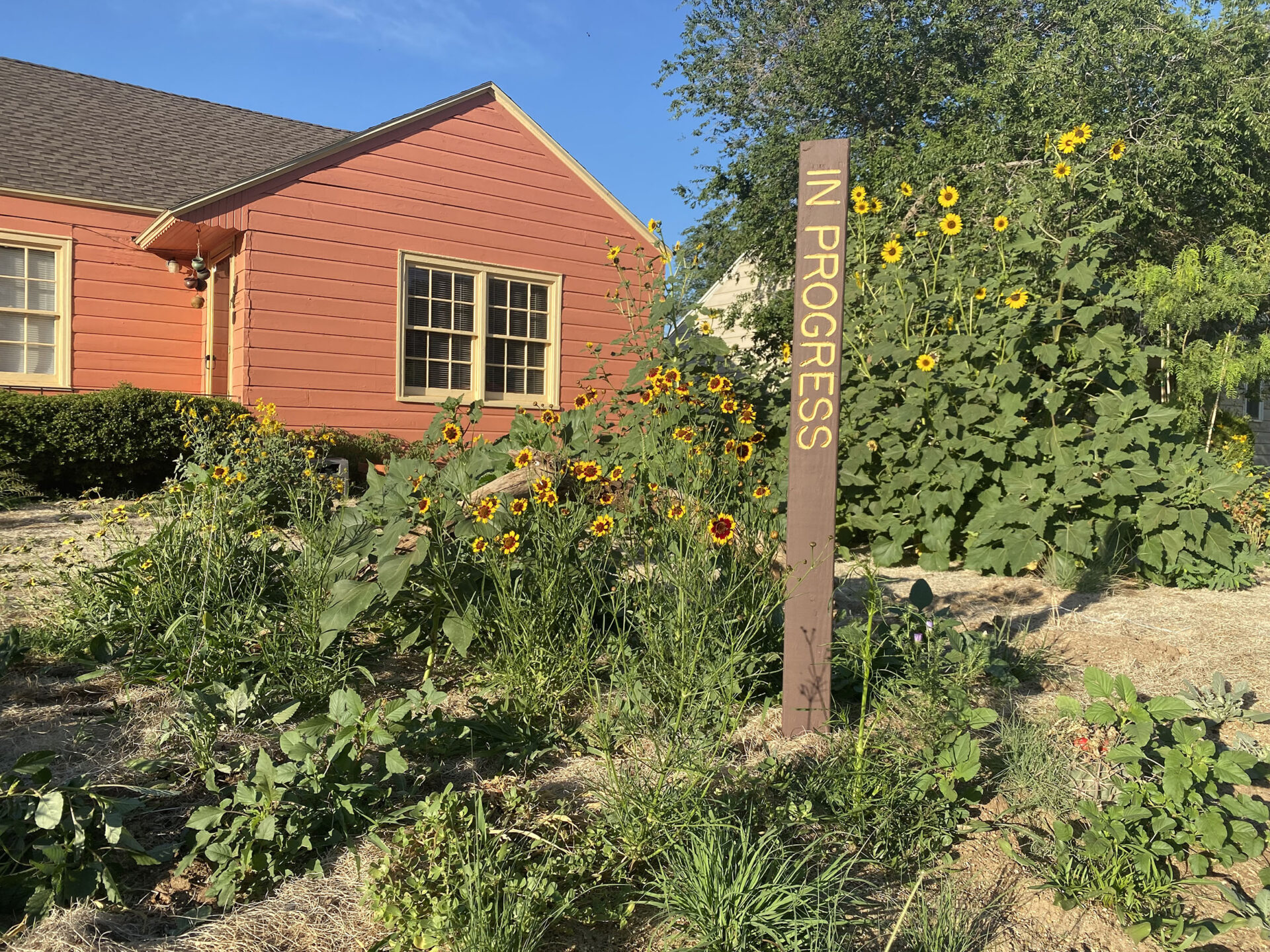 A red building set among flowering plants with a sign that says