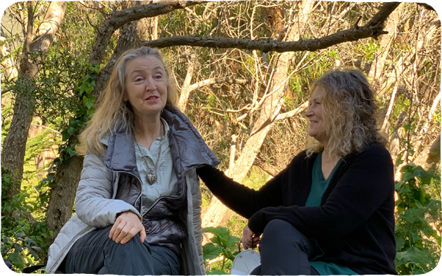 Holly Blake and Rebecca Solnit, sitting beneath some trees talking with one another.