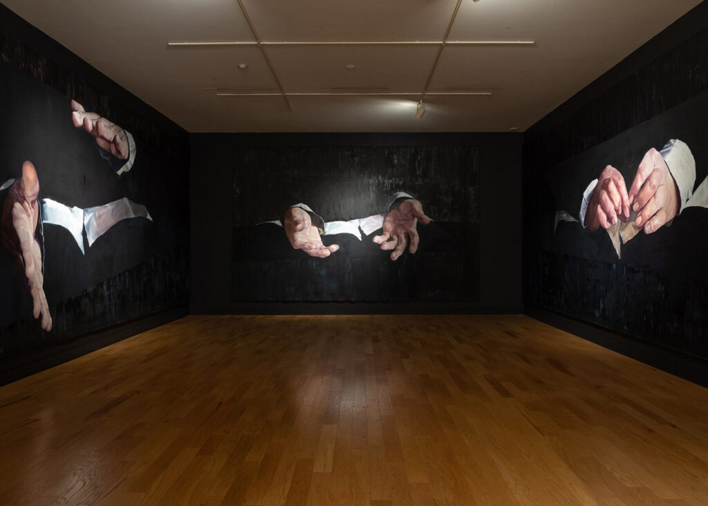 A large gallery, three walls visible, each painted with image of outstretched hands