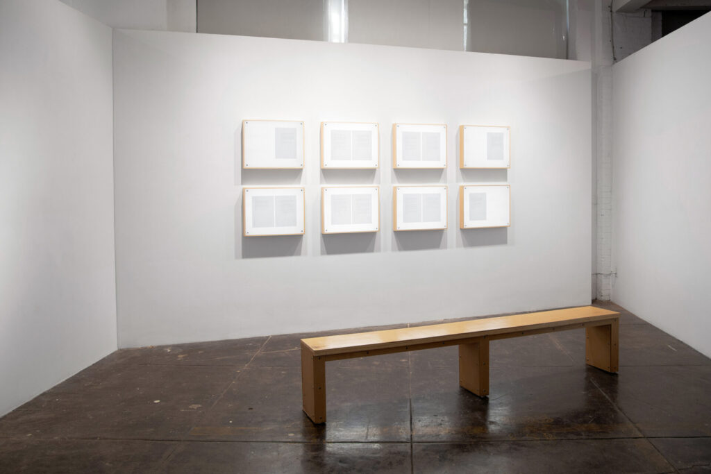 An exhibition room with a low table and a wall of type written pages in frames