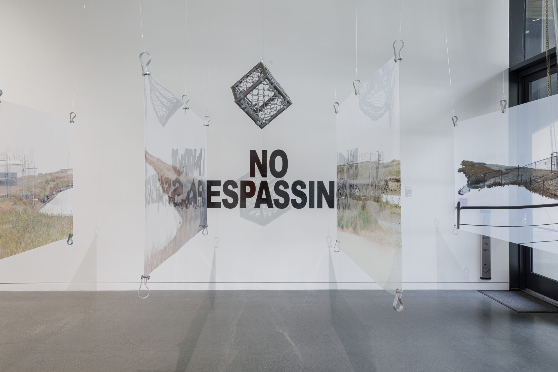 Photographs printed on transparency suspended in a gallery with text that reads