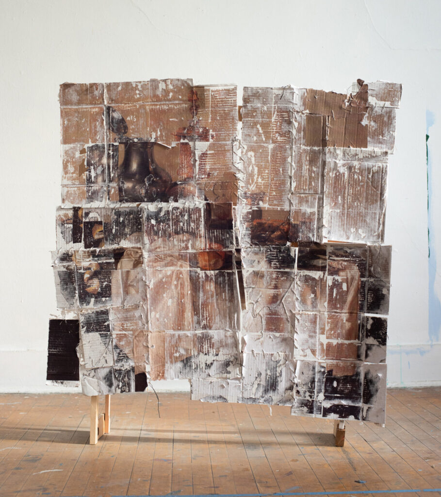 A collage of cardboard and other materials with images hanging from a wood structure.
